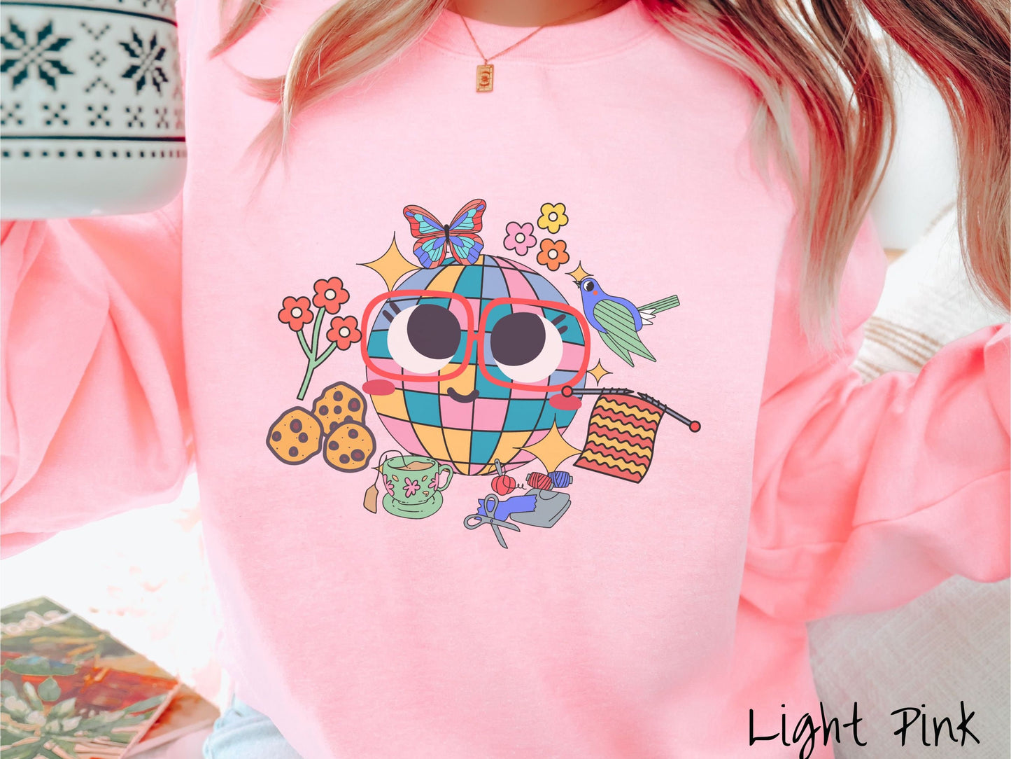 A woman wearing a cute light pink colored sweatshirt with a femsale face wearing glasses and smiling