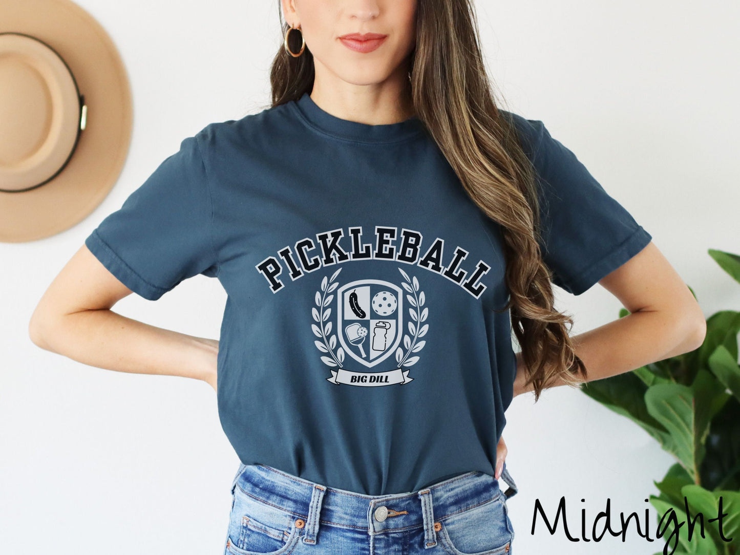 A woman wearing a cute midnight colored shirt with the text Pickleball across the top, a varsity logo centered underneath, and the words Big Dill underneath the logo.