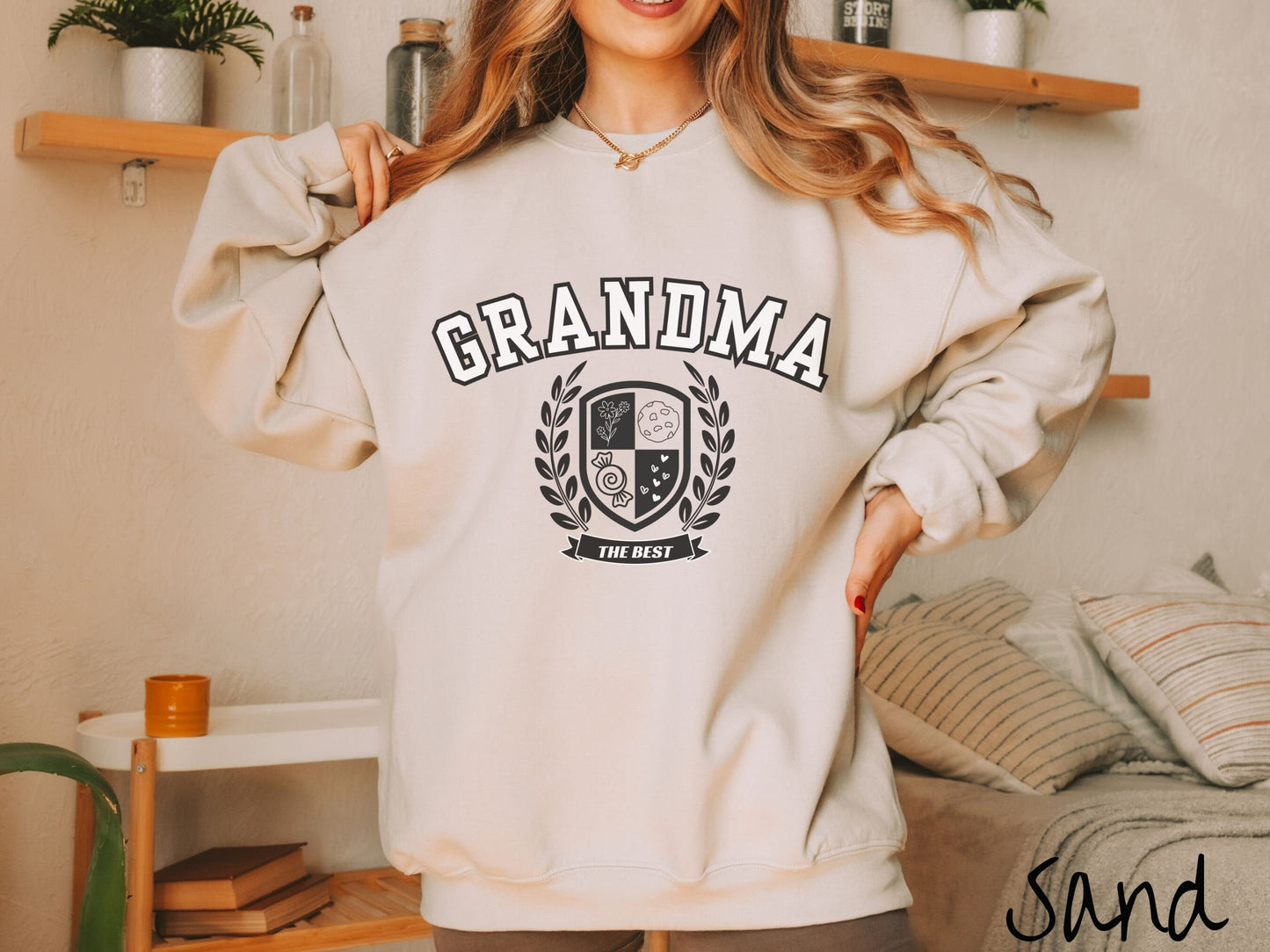 A woman wearing a cute sand colored sweatshirt with text saying Grammy across the front with a varsity logo underneath with the words The Best centered underneath the logo.
