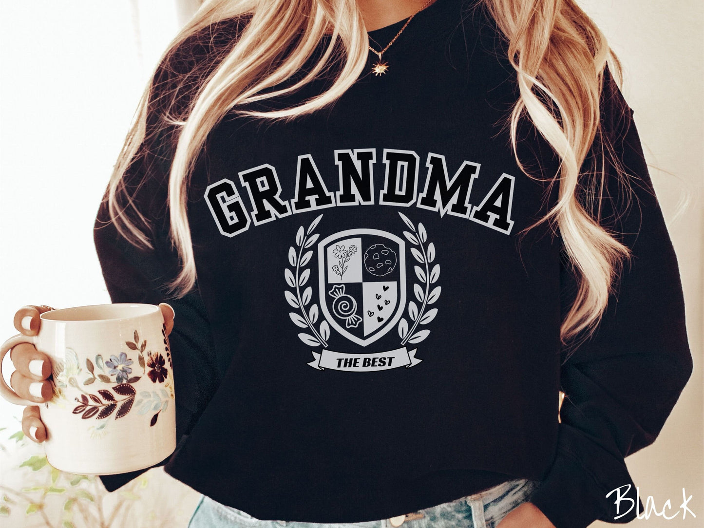 A woman wearing a cute black colored sweatshirt with text saying Grammy across the front with a varsity logo underneath with the words The Best centered underneath the logo.
