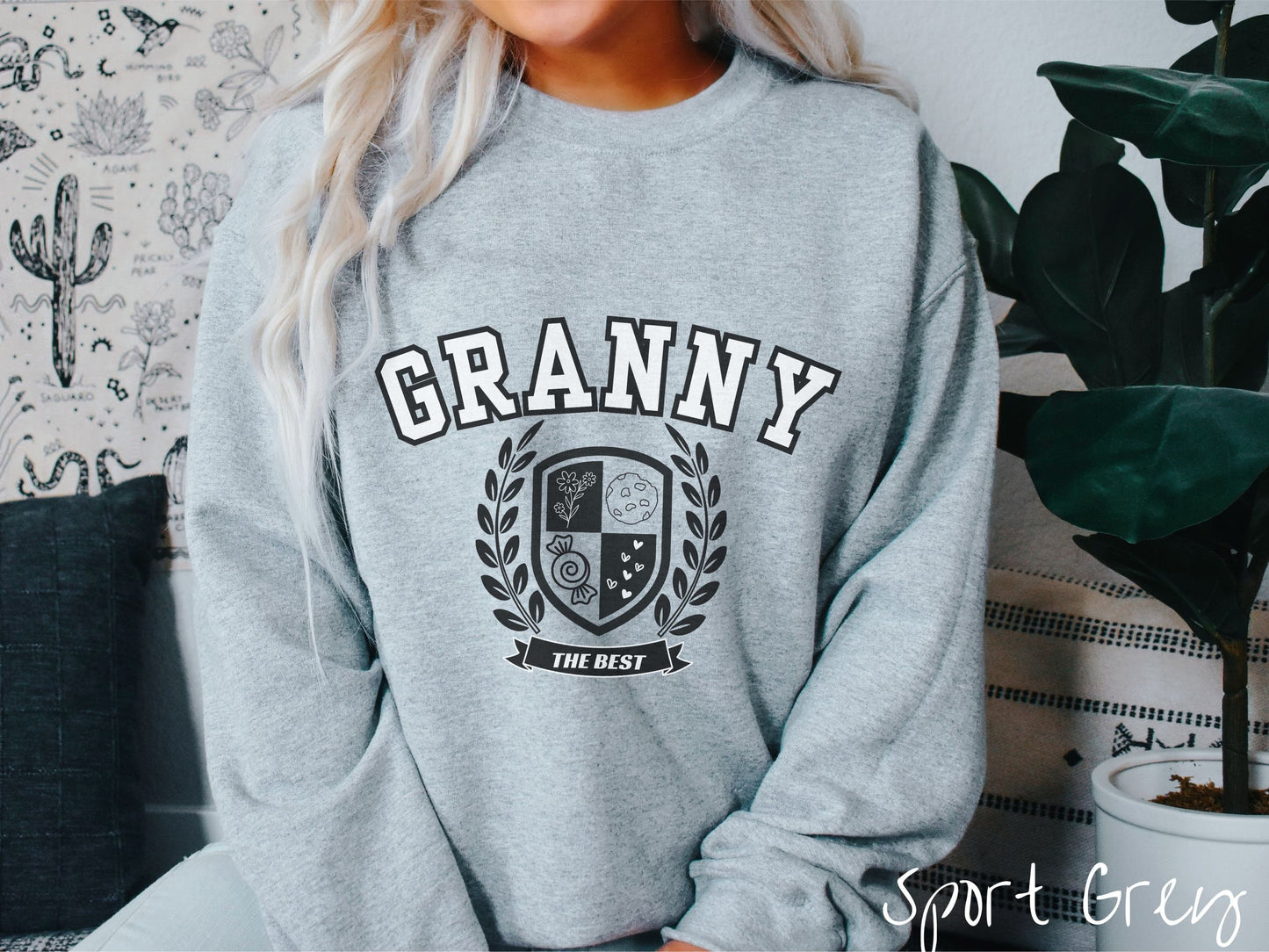 A woman wearing a cute sport grey colored sweatshirt with text saying Granny across the front with a varsity logo underneath with the words The Best centered underneath the logo.
