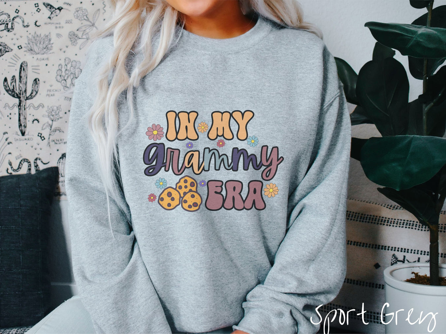 A woman wearing a cute gray sweatshirt with the text saying In My Grammy era with flowers and chocolate chip cookies mixed within the text.