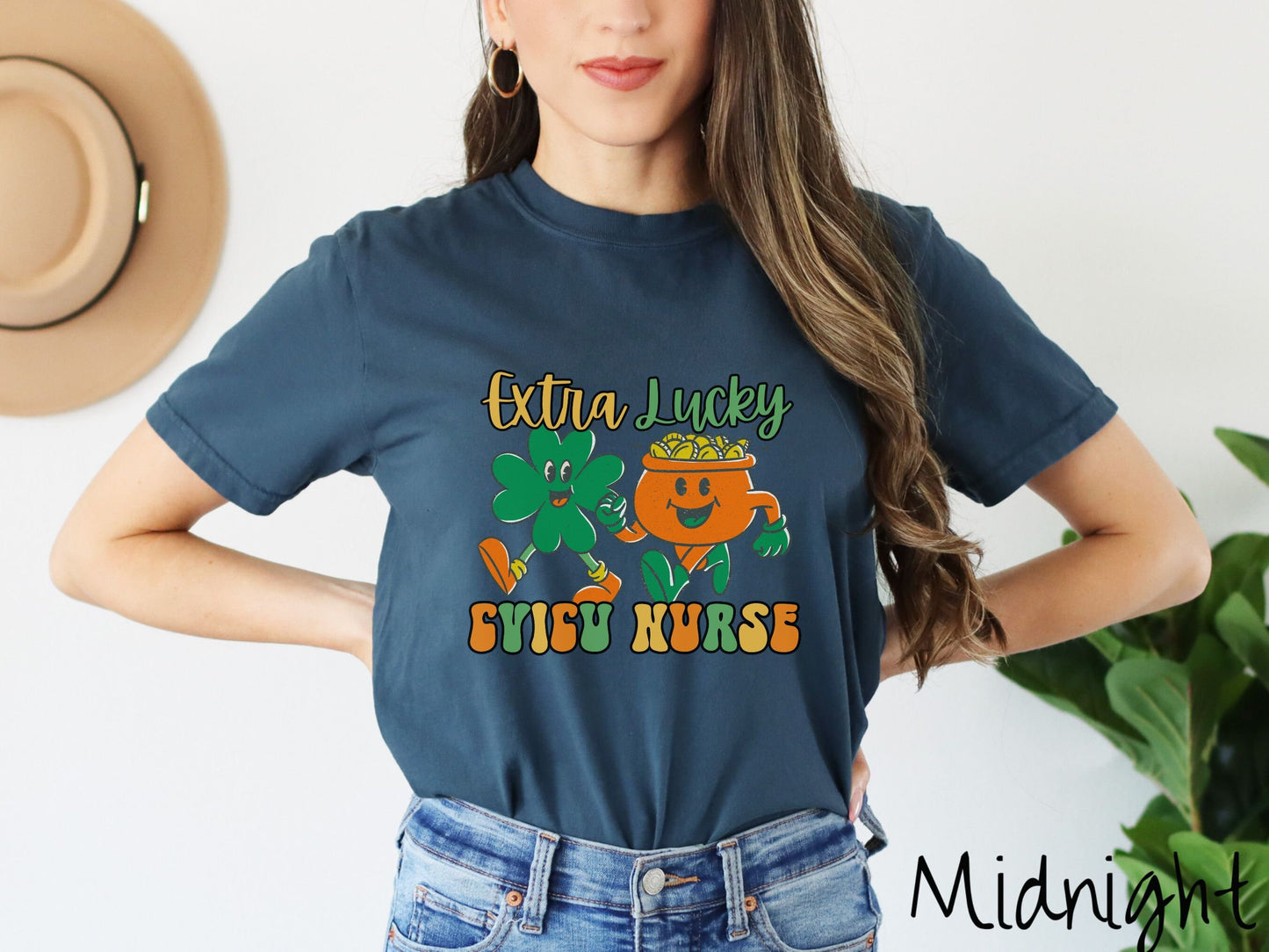 A woman wearing a vintage, midnight colored shirt with the text Extra Lucky CVICU Nurse in yellow, orange, and green font. Between the text are a green clover and orange pot of gold smiling and walking together in step.
