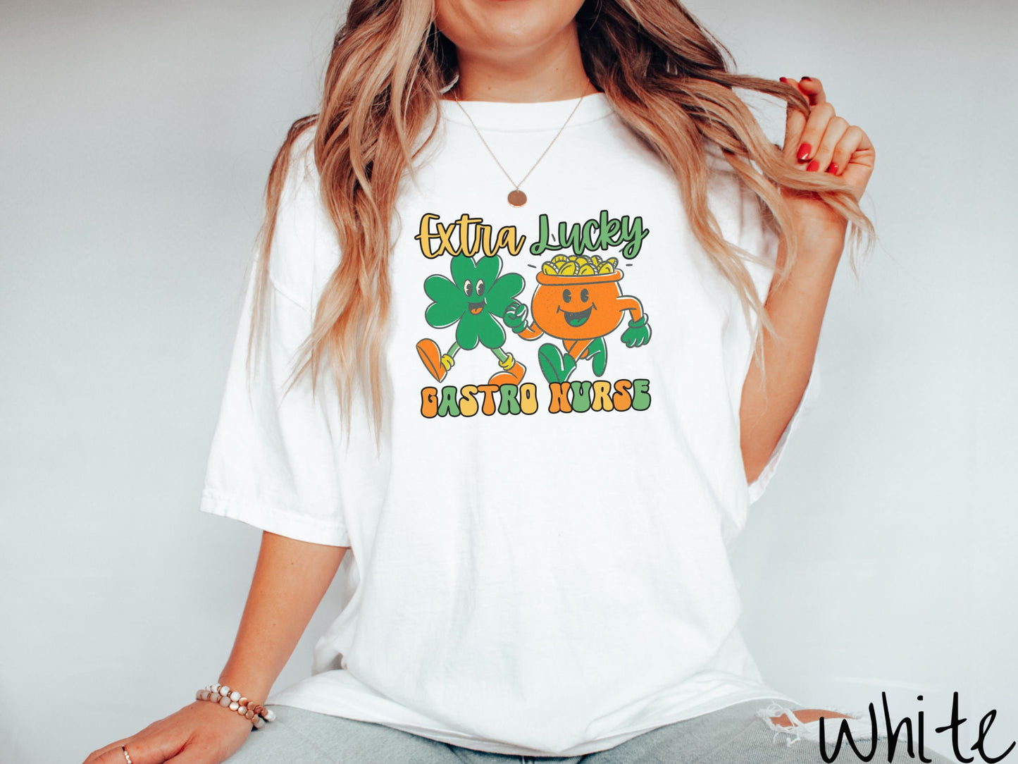 A woman wearing a vintage, white colored shirt with the text Extra Lucky Gastro Nurse in yellow, orange, and green font. Between the text are a green clover and orange pot of gold smiling and walking together in step.
