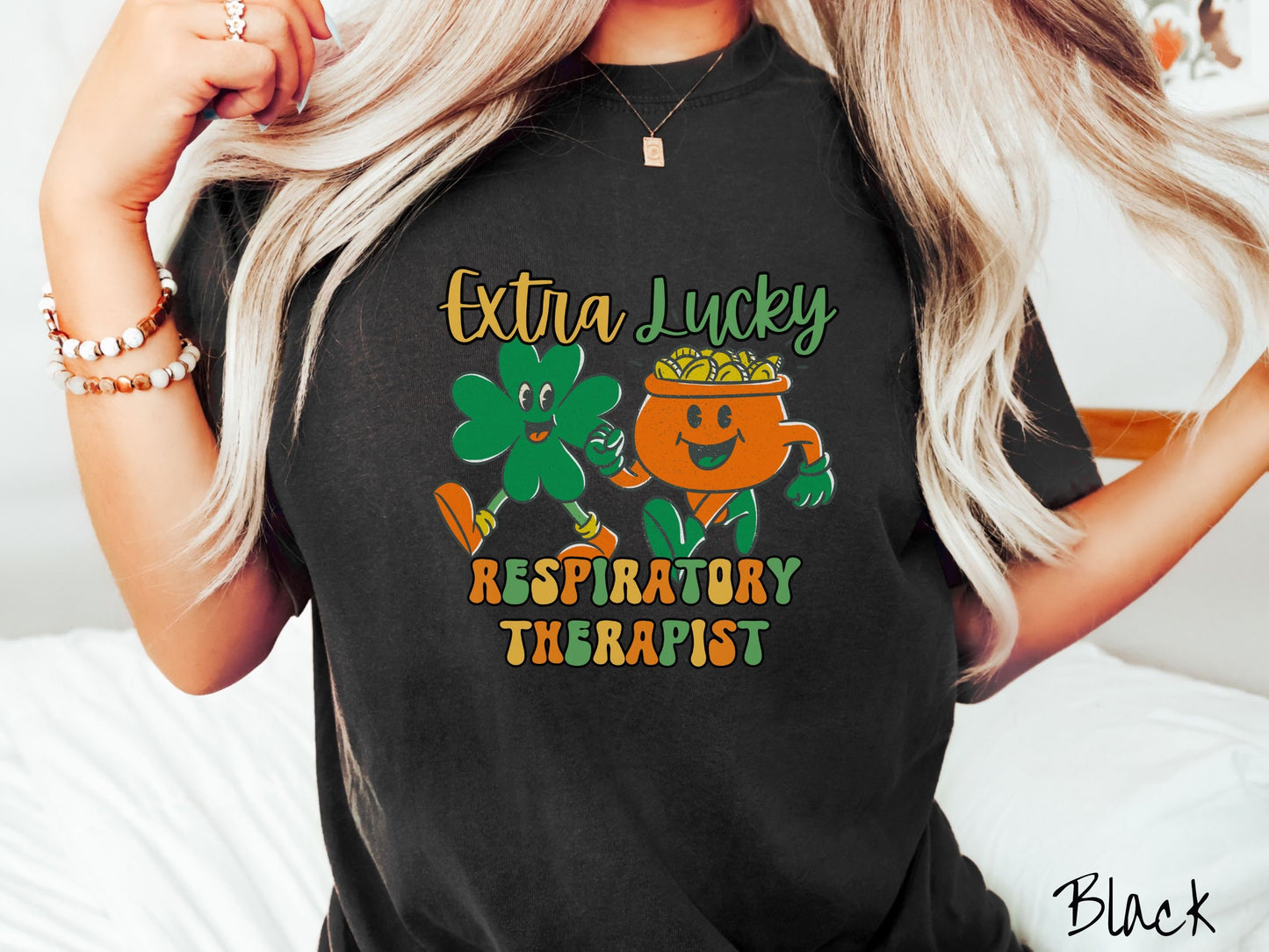 A woman wearing a vintage, black colored shirt with the text Extra Lucky Respiratory Therapist in yellow, orange, and green font. Between the text are a green clover and orange pot of gold smiling and walking together in step.
