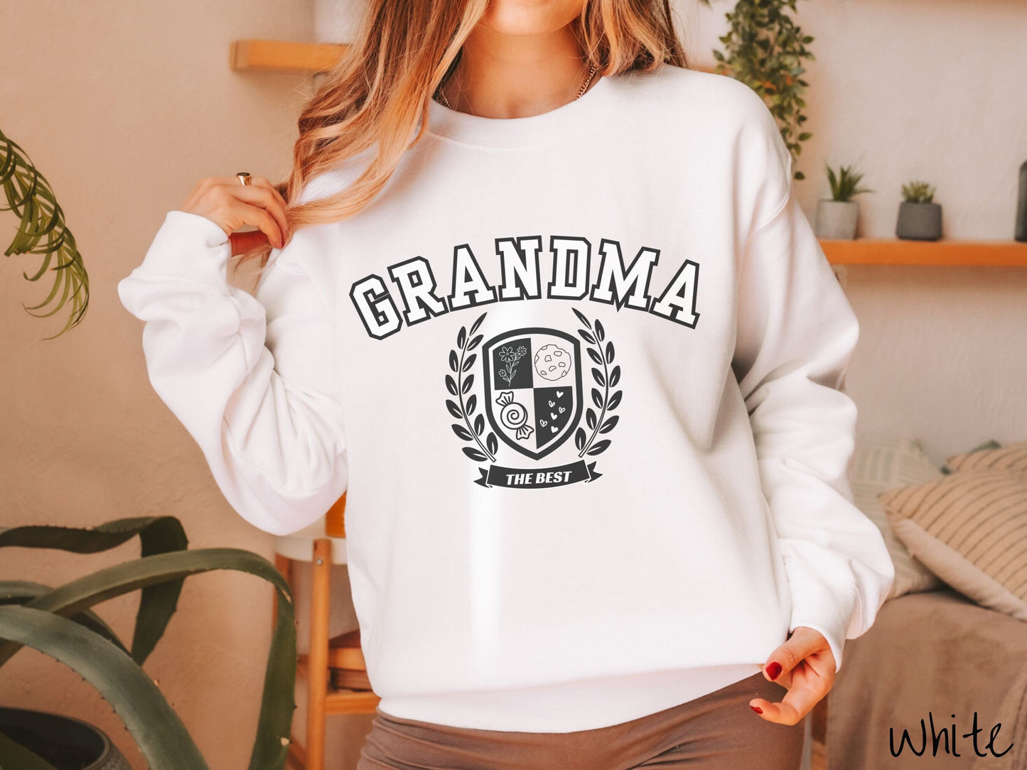 A woman wearing a cute white colored sweatshirt with text saying Grammy across the front with a varsity logo underneath with the words The Best centered underneath the logo.