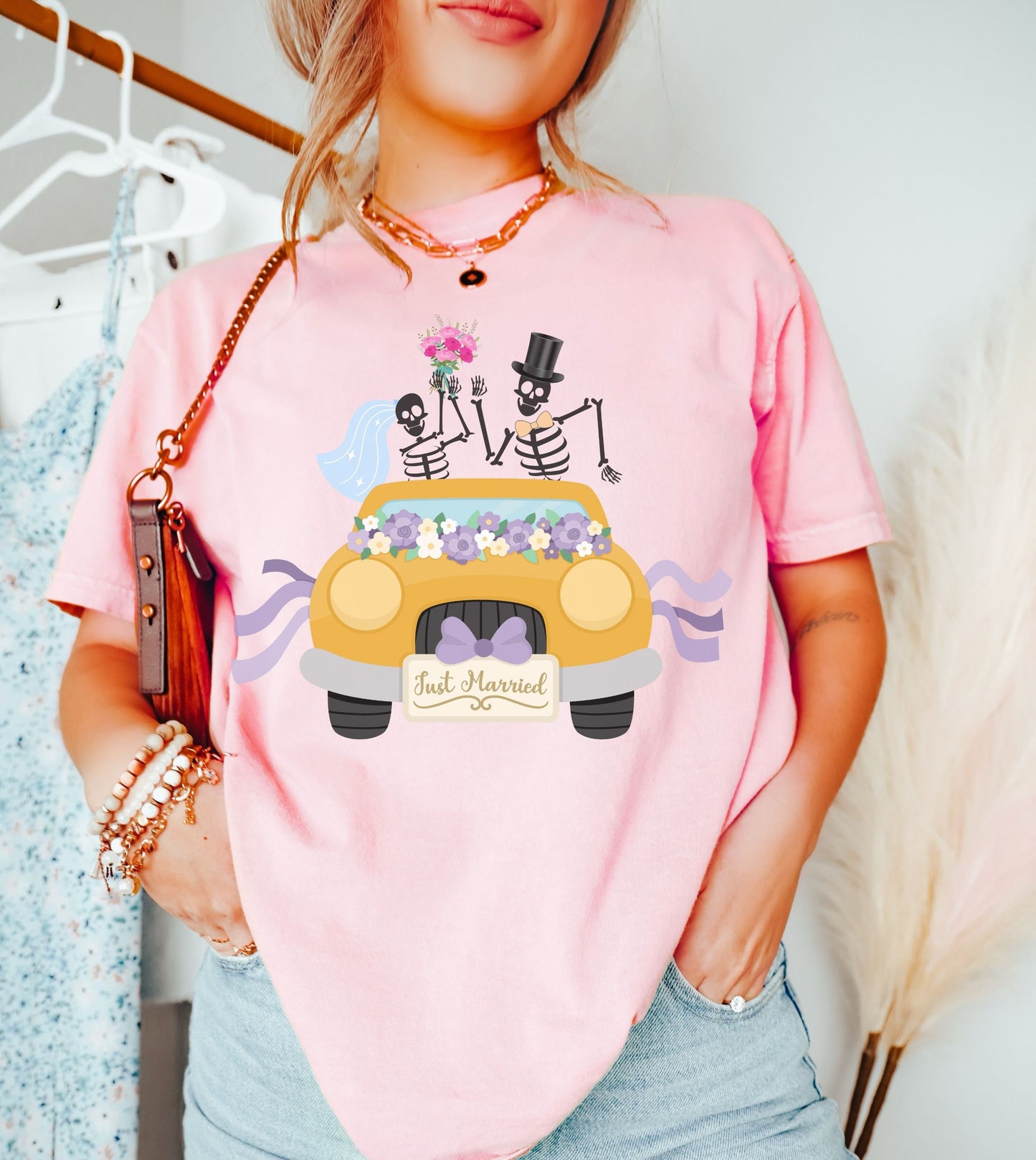 A woman wearing a cute light pink colored shirt with a newlywed couple holding flowers and waving goodbye from a gold colored car with the text Just Married on the front of the vehicle.