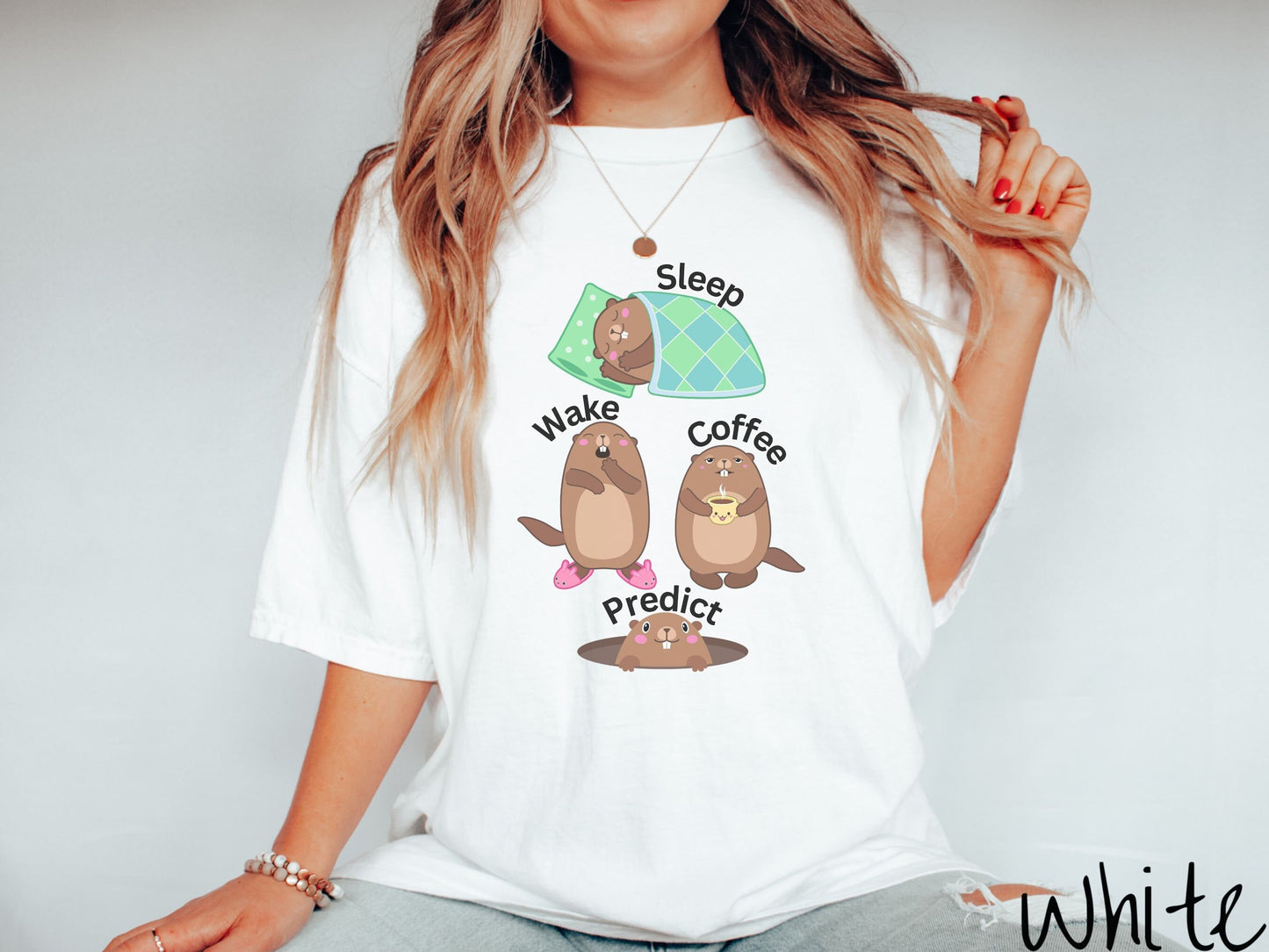 A woman wearing a cute white colored shirt with the text Sleep, Wake, Coffee, and Predict accompanied with pictures of a groundhog sleeping, a groundhog waking up yawning, one holding a steaming cup of coffee, and another exiting its hole.