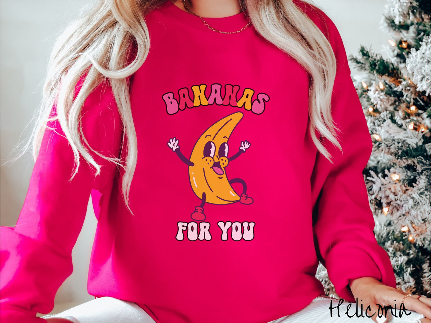 A woman wearing a cute, vintage heliconia colored sweatshirt with the text Bananas for You in pink, red, purple, and white colors, and a cheerful banana with its arms open and a smiling face in the middle of the text.