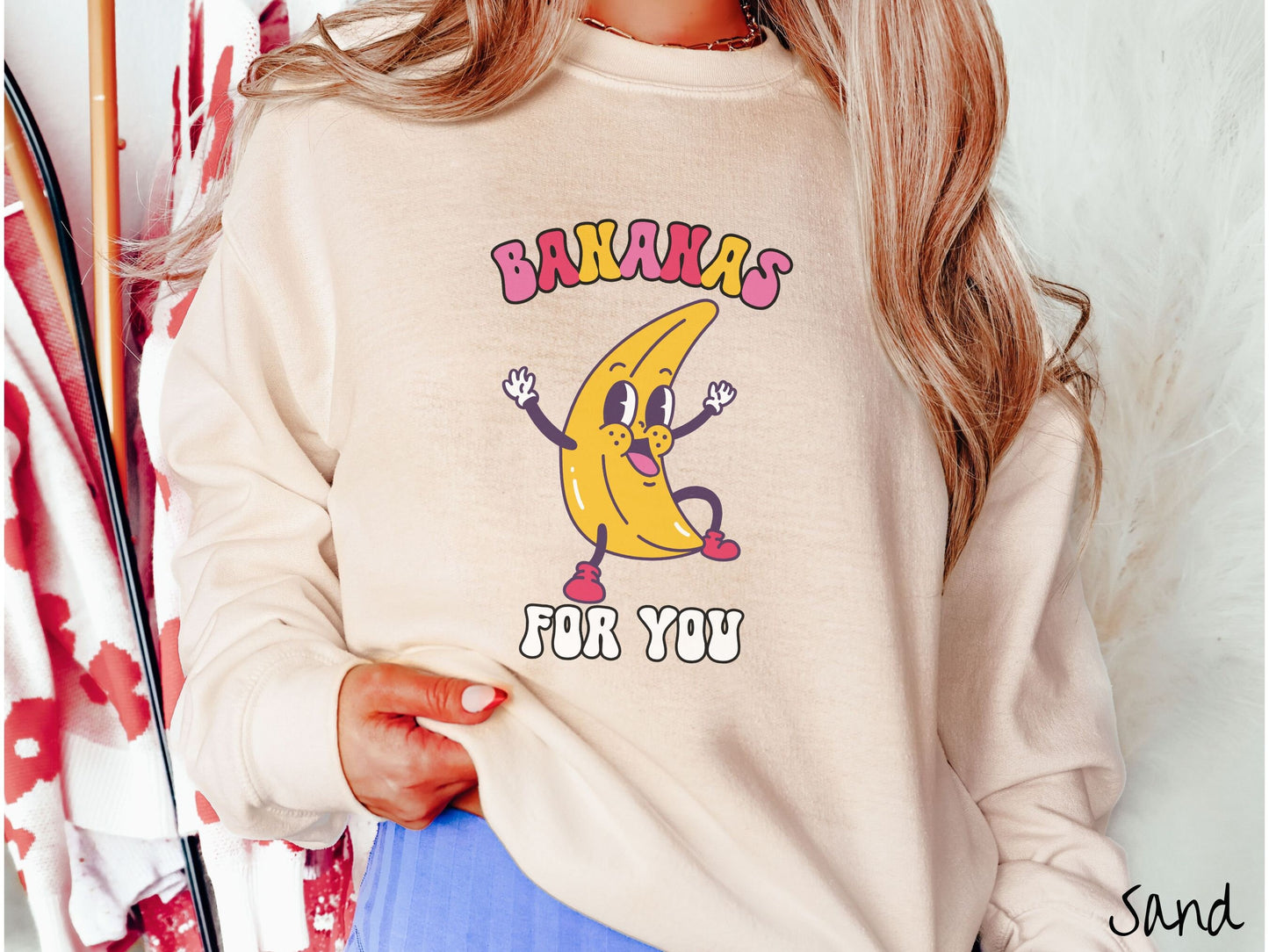 A woman wearing a cute, vintage sand colored sweatshirt with the text Bananas for You in pink, red, purple, and white colors, and a cheerful banana with its arms open and a smiling face in the middle of the text.