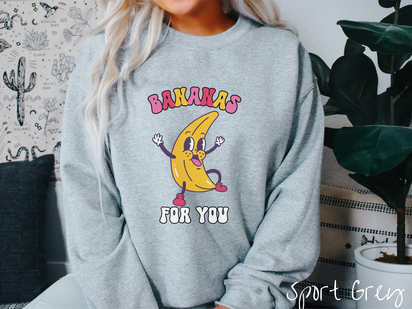 A woman wearing a cute, vintage sport grey colored sweatshirt with the text Bananas for You in pink, red, purple, and white colors, and a cheerful banana with its arms open and a smiling face in the middle of the text.