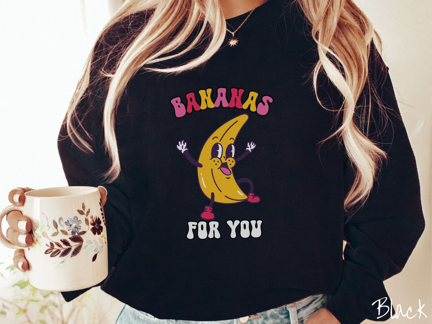 A woman wearing a cute, vintage black colored sweatshirt with the text Bananas for You in pink, red, purple, and white colors, and a cheerful banana with its arms open and a smiling face in the middle of the text.