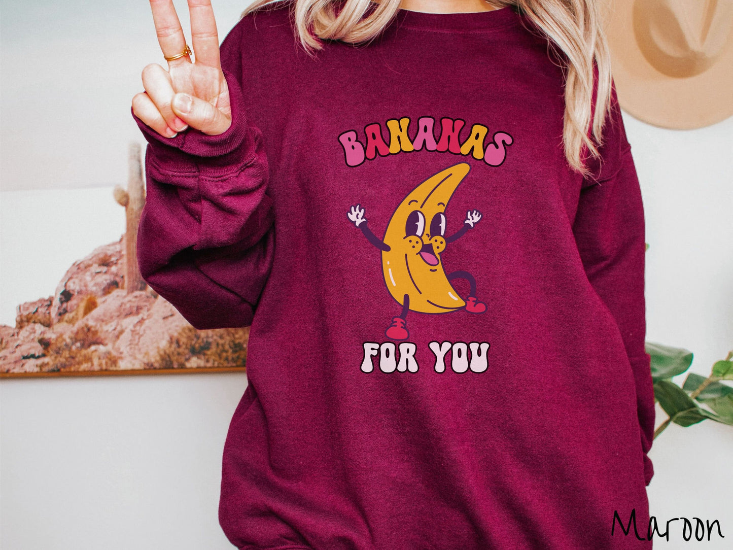A woman wearing a cute, vintage maroon colored sweatshirt with the text Bananas for You in pink, red, purple, and white colors, and a cheerful banana with its arms open and a smiling face in the middle of the text.
