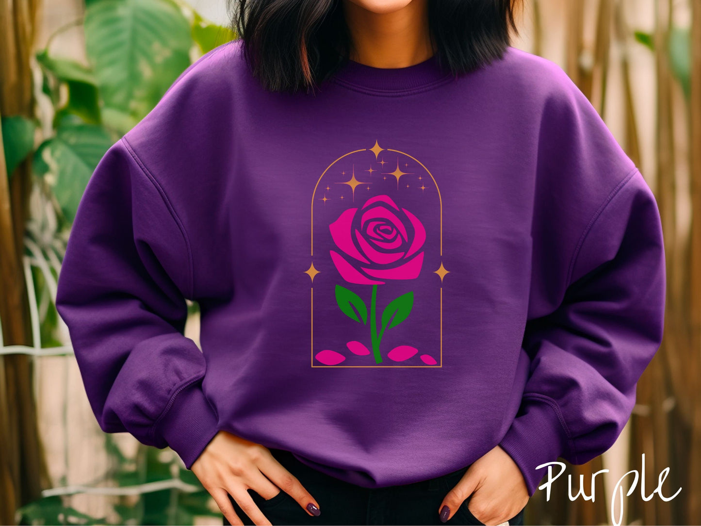 A woman wearing a cute, vintage purple colored sweatshirt with an enchanted pink rose in a golden clear container with gold stars twinkling above and pink flower petals resting below.
