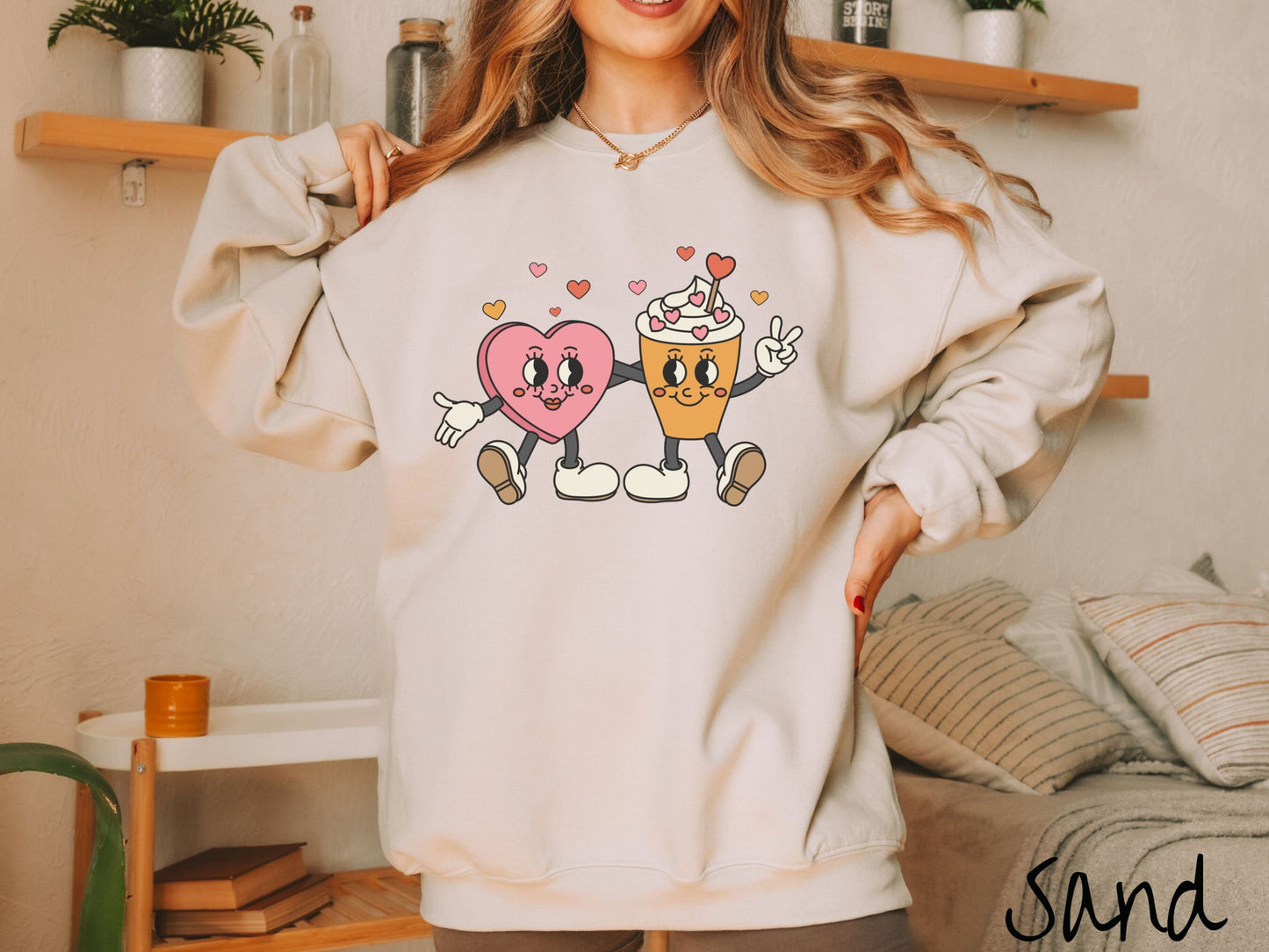 A woman wearing a cute, vintage sand colored sweatshirt with colorful hearts above, a female heart with smiling face, legs, and arms wrapping her left arm around a whipped cream topped light brown coffee cup with a heart-tipped topper.