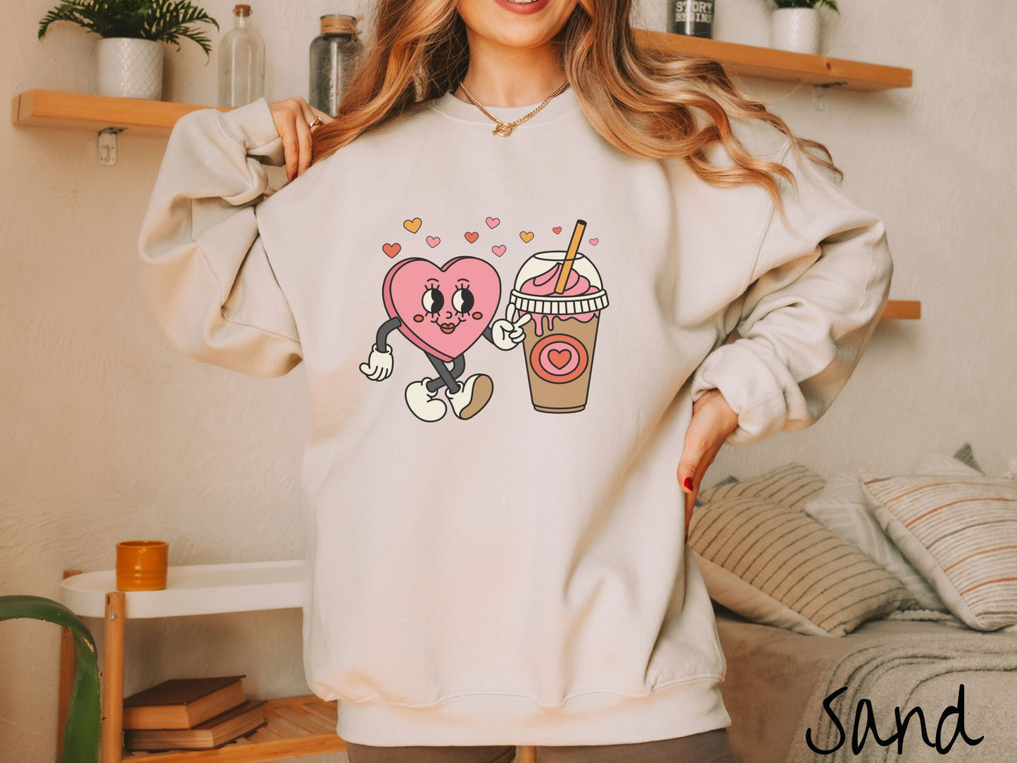 A woman wearing a cute, vintage sand colored sweatshirt and colorful hearts above, a female heart with smiling face, legs, and arms showing a peace sign with her left hand next to an iced coffee and pink whipped cream and a red heart logo on the cup.