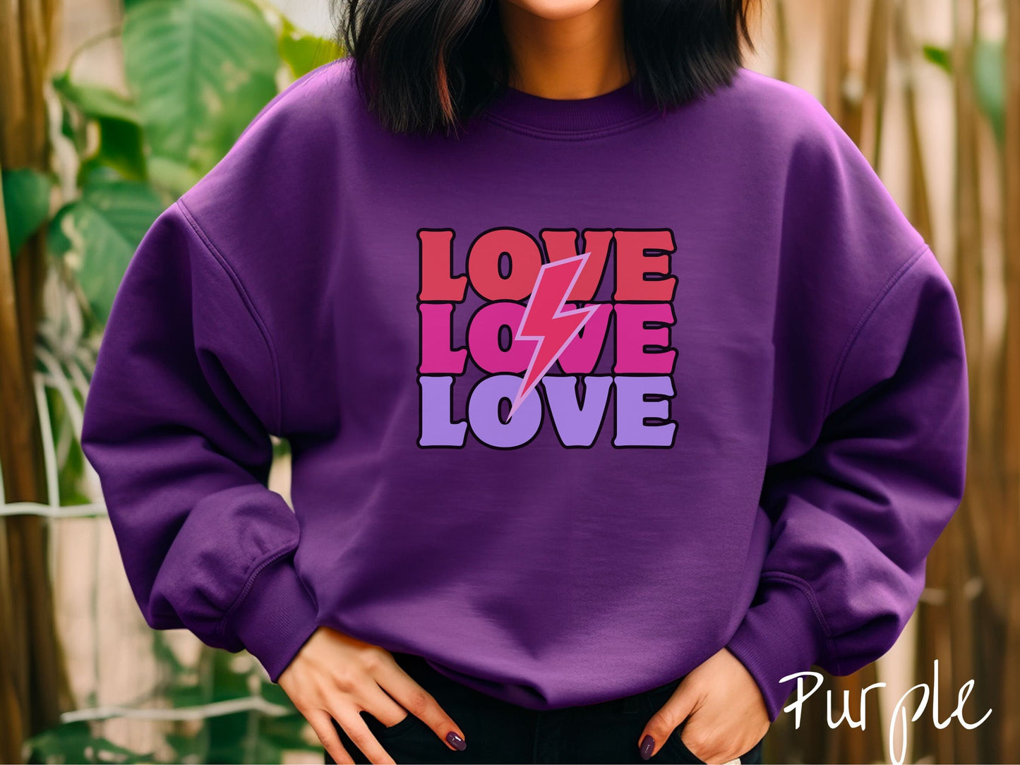 A woman wearing a cute, vintage purple colored sweatshirt with the word Love listed three times vertically with a pink lightning bolt going through the middle of the words.
