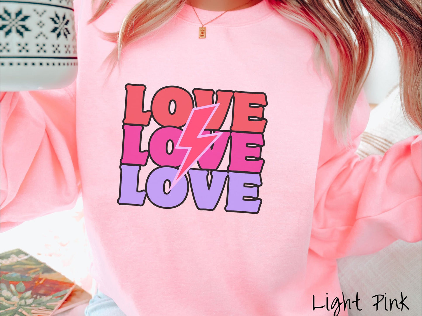 A woman wearing a cute, vintage light pink colored sweatshirt with the word Love listed three times vertically with a pink lightning bolt going through the middle of the words.