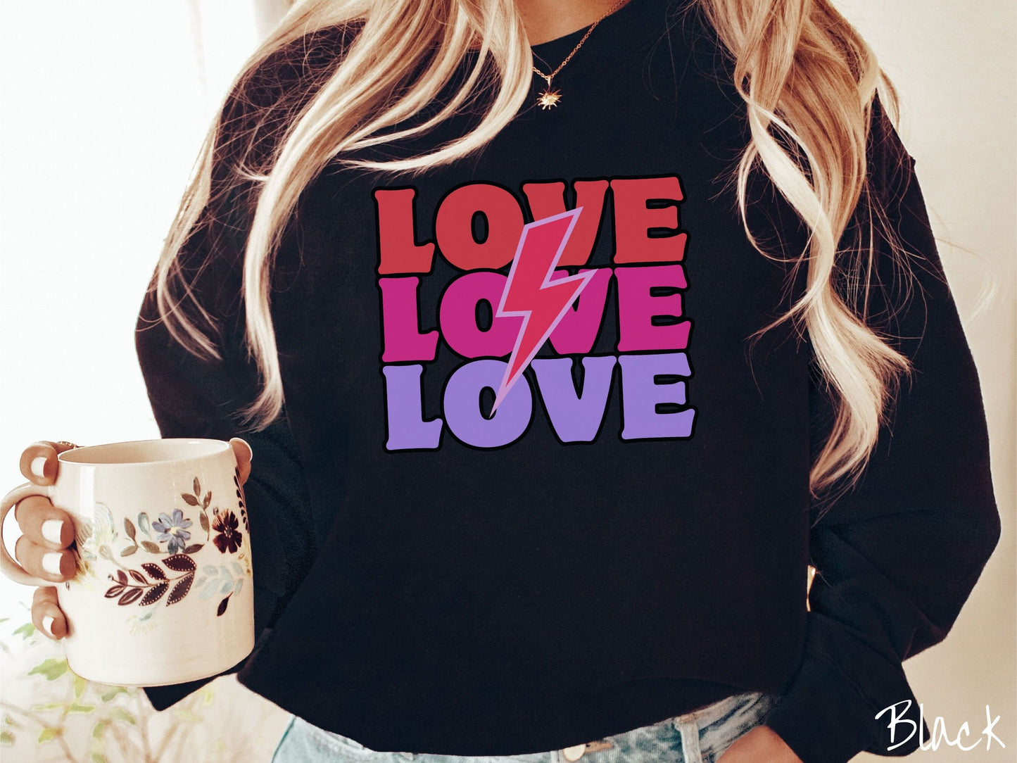 A woman wearing a cute, vintage black colored sweatshirt with the word Love listed three times vertically with a pink lightning bolt going through the middle of the words.
