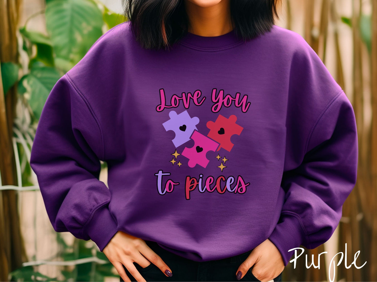 A woman wearing a cute, vintage purple colored sweatshirt with the text Love you to pieces in red, pink, and purple colors, and three red, pink, and purple puzzle pieces with hearts on them surrounded by yellow stars.