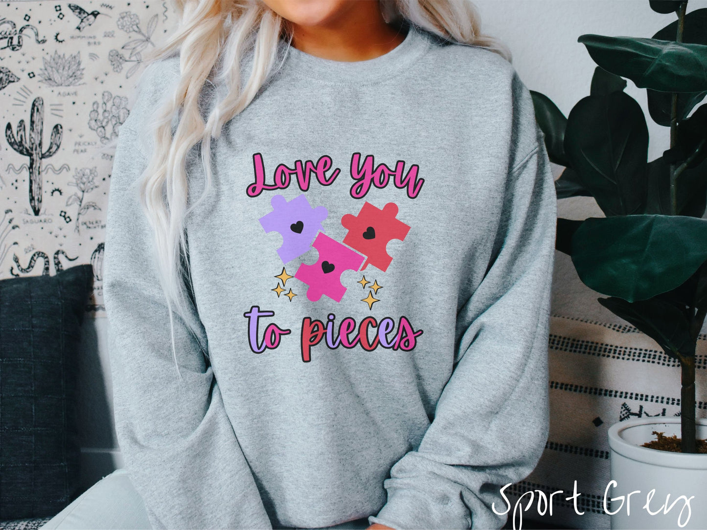 A woman wearing a cute, vintage sport grey colored sweatshirt with the text Love you to pieces in red, pink, and purple colors, and three red, pink, and purple puzzle pieces with hearts on them surrounded by yellow stars.