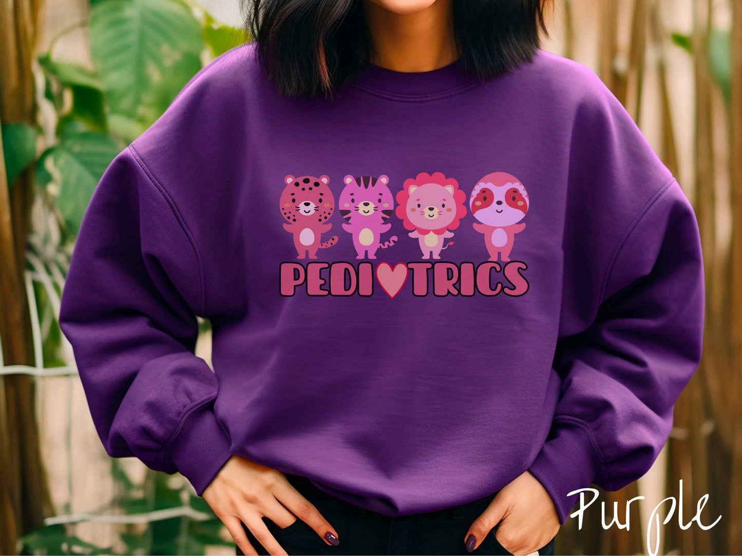 A woman wearing a cute purple colored sweatshirt with the text Pediatrics in the center, a heart replacing the letter A, and above the text are a maroon lion, a pink tiger, a red lion, and a pink sloth all with their hands open asking for a hug.