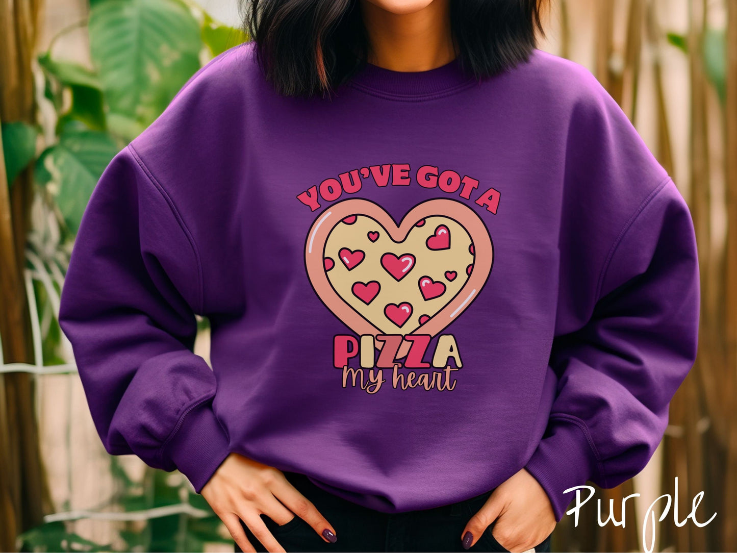 A woman wearing a cute purple colored sweatshirt with red text Youve Got a Pizza My Heart around a heart-shaped pizza with heart-shaped red pepperonis.