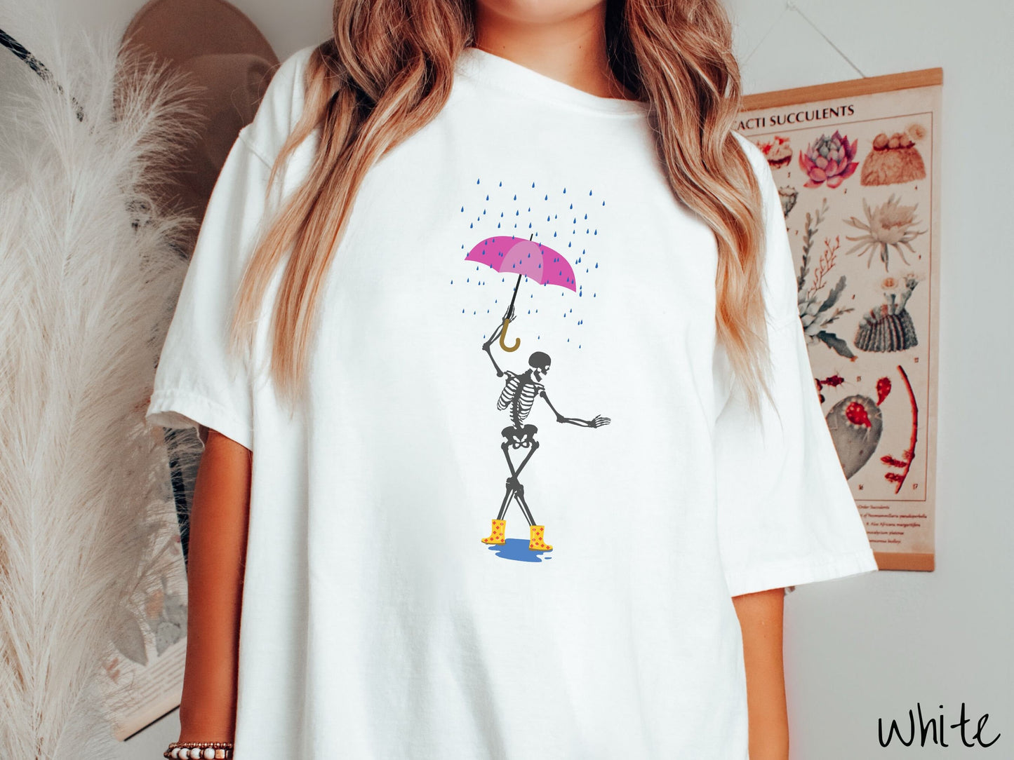A woman wearing a cute white colored shirt with a dark grey female skeleton dancing in the rain with a pink and purple umbrella and wearing yellow with red polka dot rain boots.