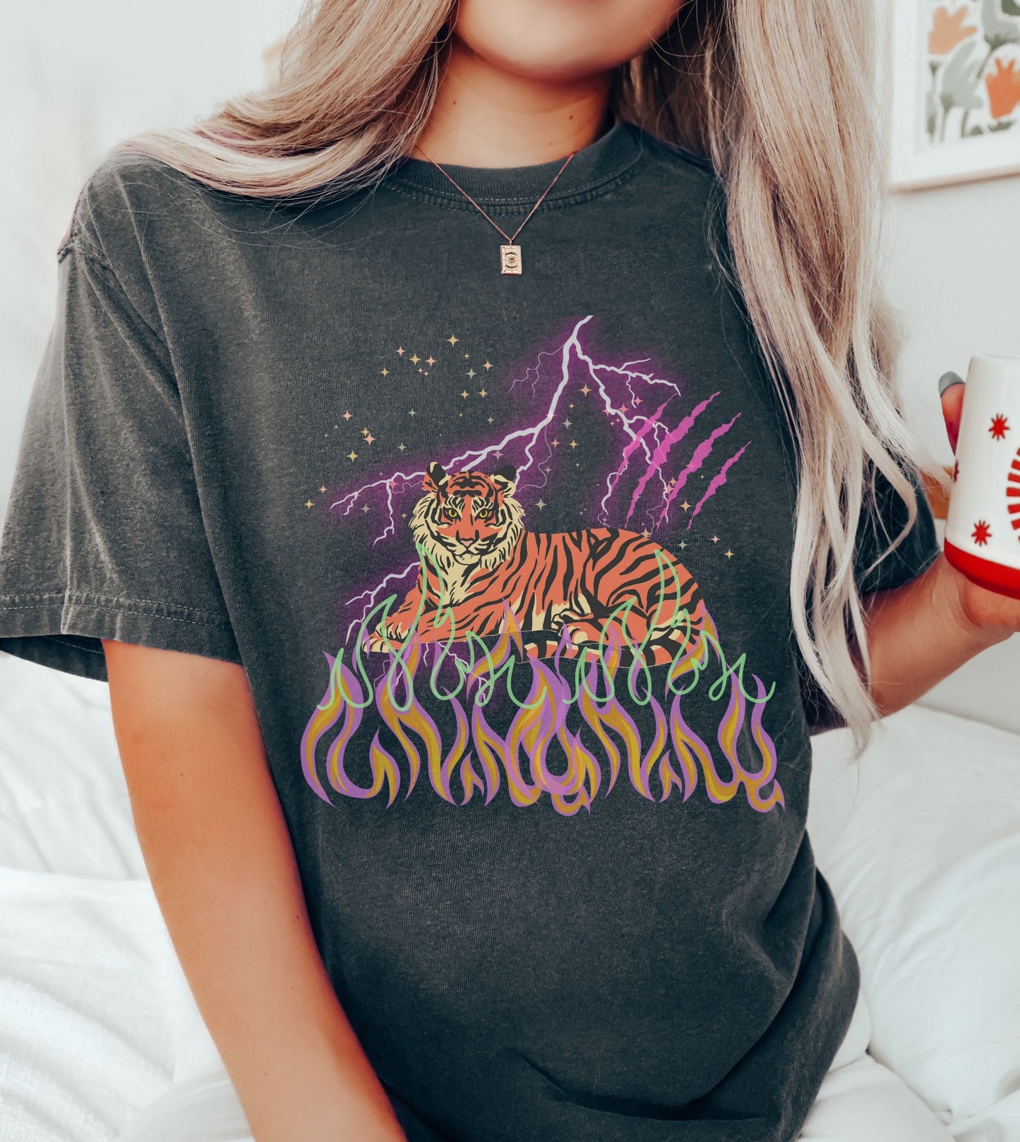 A woman wearing a vintage, pepper colored shirt with a yellow and orange tiger laying across orange and pink flames, above is purple lightning streaking across the top and a pink tiger claw scratch.