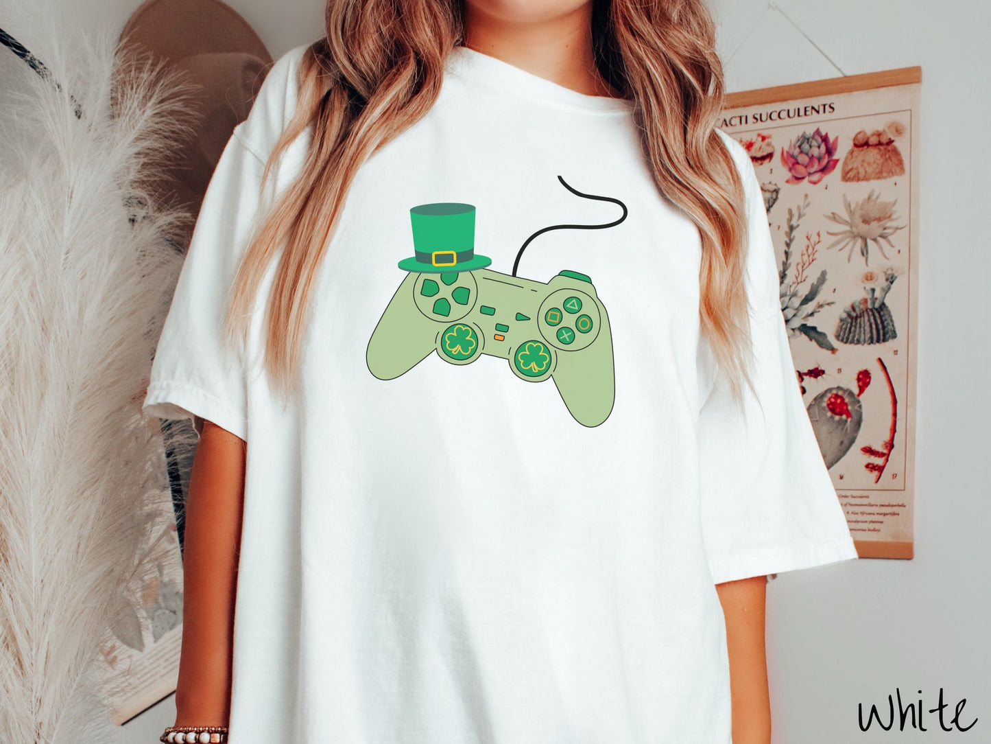 A woman wearing a vintage, white colored shirt with a black video game controller with green buttons and joysticks, the analog control sticks are in the shape of green leaf clovers, and there is a green top hat hanging off the top left trigger.