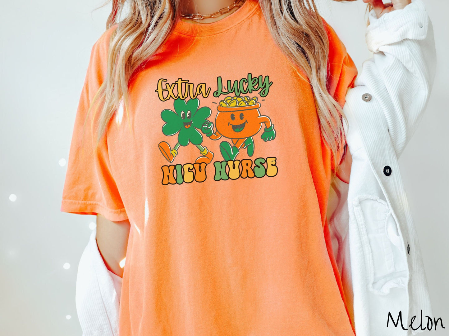 A woman wearing a vintage, melon colored shirt with the text Extra Lucky NICU Nurse in yellow, orange, and green font. Between the text are a green clover and orange pot of gold smiling and walking together in step.