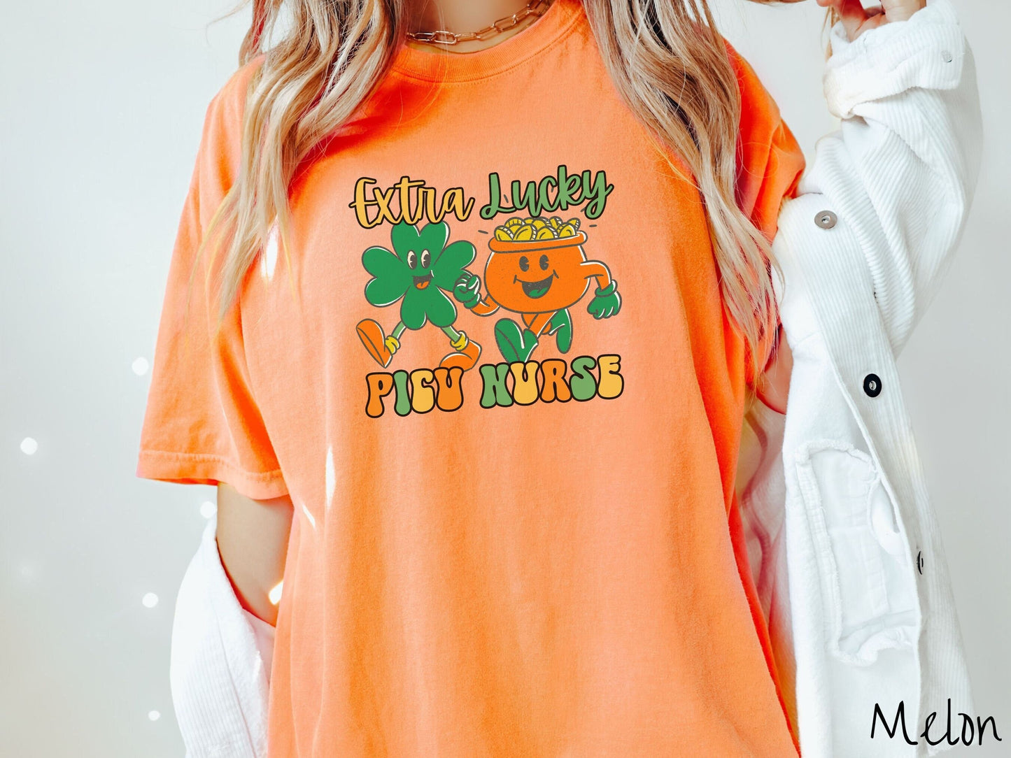 A woman wearing a vintage, melon colored shirt with the text Extra Lucky PICU Nurse in yellow, orange, and green font. Between the text are a green clover and orange pot of gold smiling and walking together in step.
