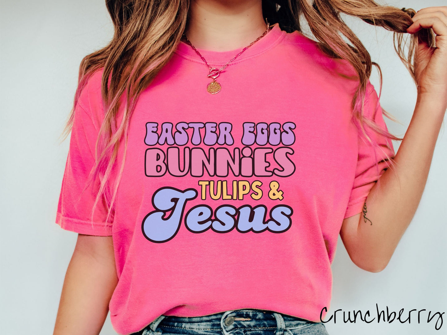 A woman wearing a cute, vintage crunchberry colored shirt with text Easter Eggs, Bunnies, Tulips, & Jesus in purple, pink, yellow, and blue font.