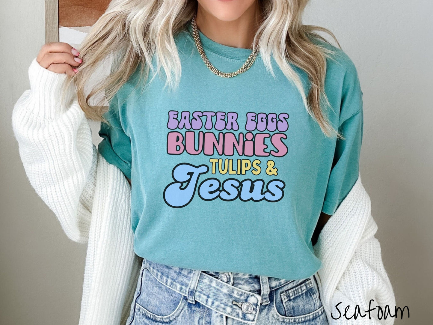 A woman wearing a cute, vintage seafoam colored shirt with text Easter Eggs, Bunnies, Tulips, & Jesus in purple, pink, yellow, and blue font.