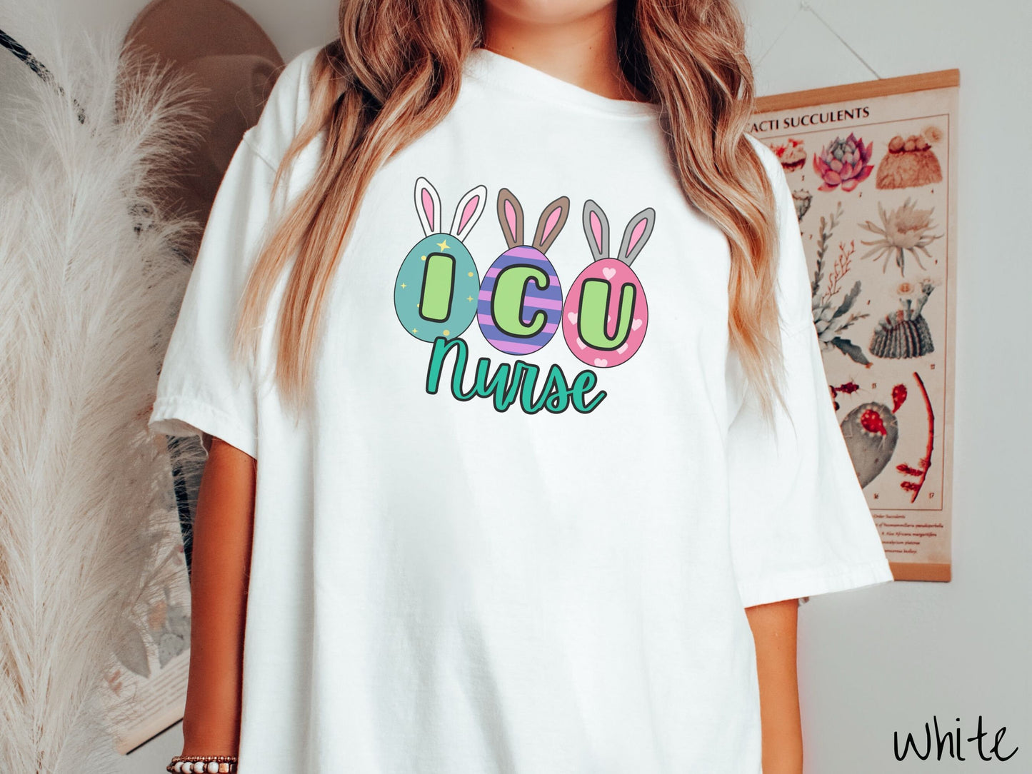 A woman wearing a cute, vintage white colored shirt with three colorful easter eggs next to each other with the letters I, C, and U inside. Each egg has a pair of bunny rabbit ears, one is white, the middle brown, and the left gray.