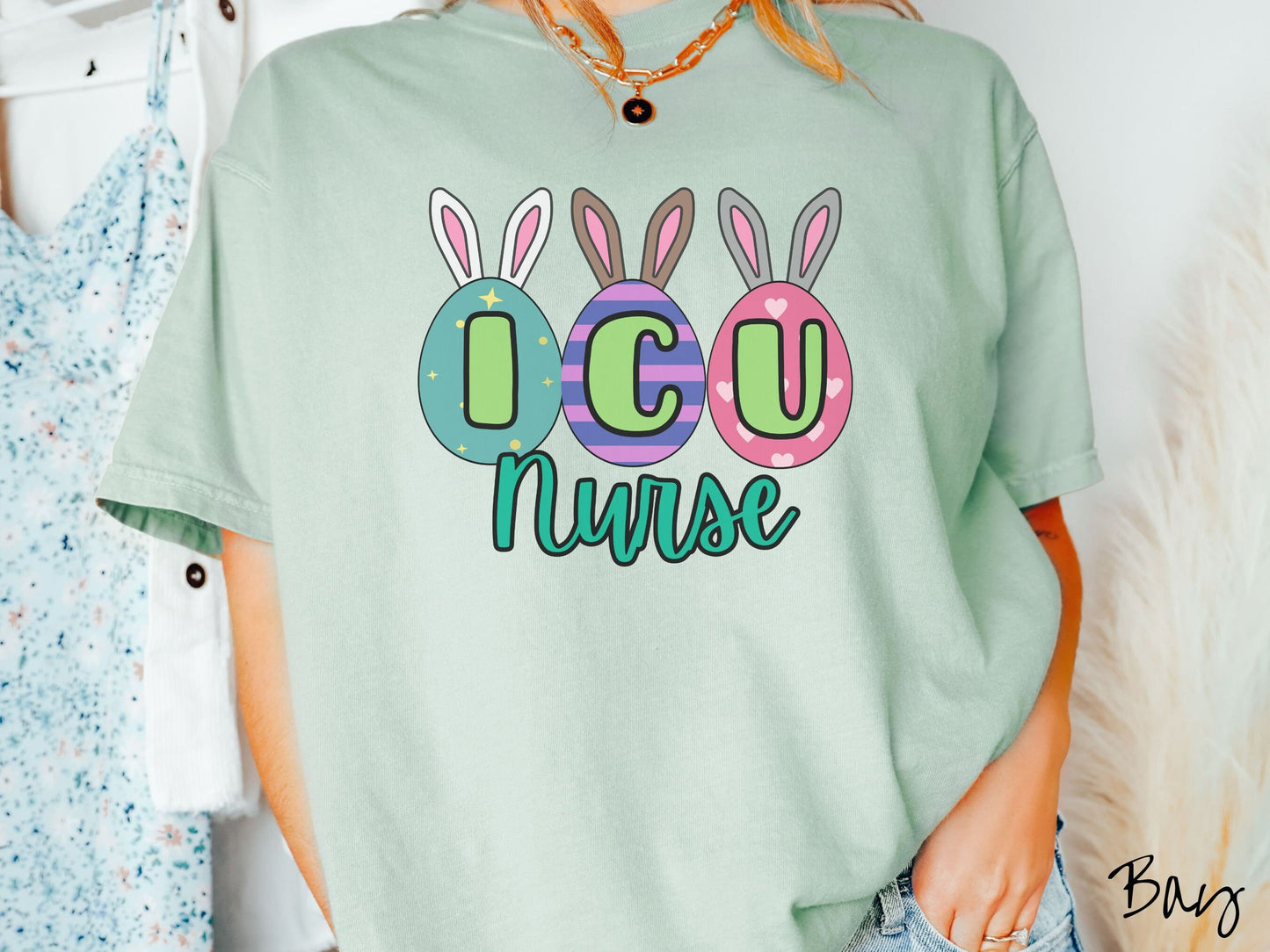 A woman wearing a cute, vintage bay colored shirt with three colorful easter eggs next to each other with the letters I, C, and U inside. Each egg has a pair of bunny rabbit ears, one is white, the middle brown, and the left gray.