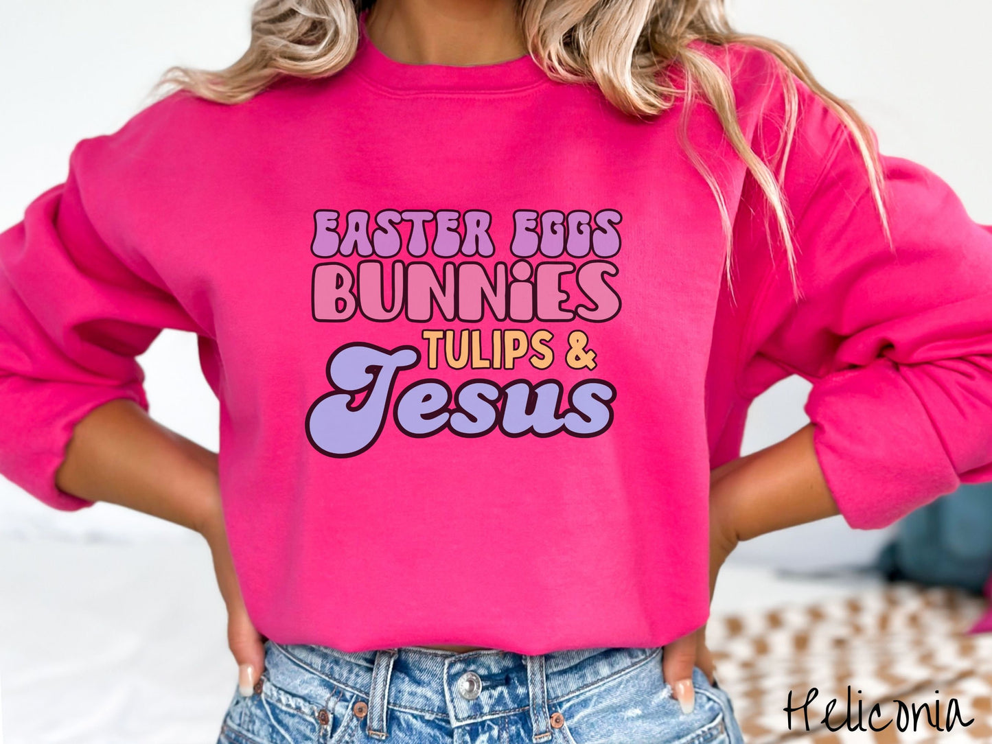 A woman wearing a cute, vintage heliconia colored sweatshirt with text Easter Eggs, Bunnies, Tulips, & Jesus in purple, pink, yellow, and blue font.