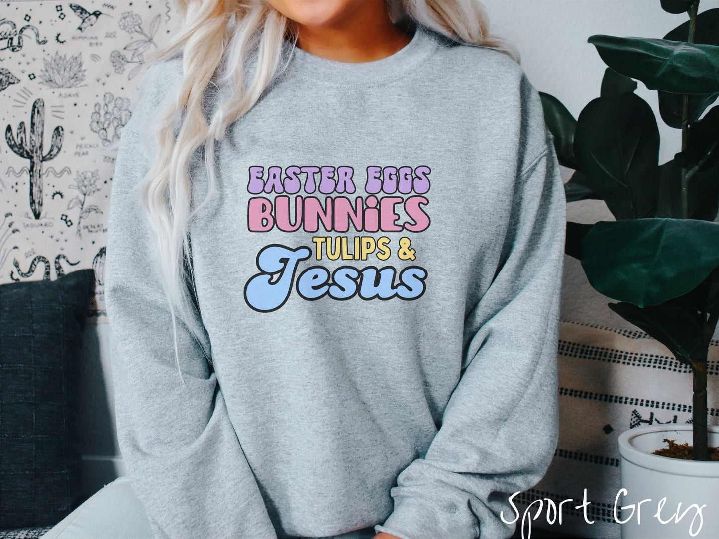 A woman wearing a cute, vintage sport grey colored sweatshirt with text Easter Eggs, Bunnies, Tulips, & Jesus in purple, pink, yellow, and blue font.