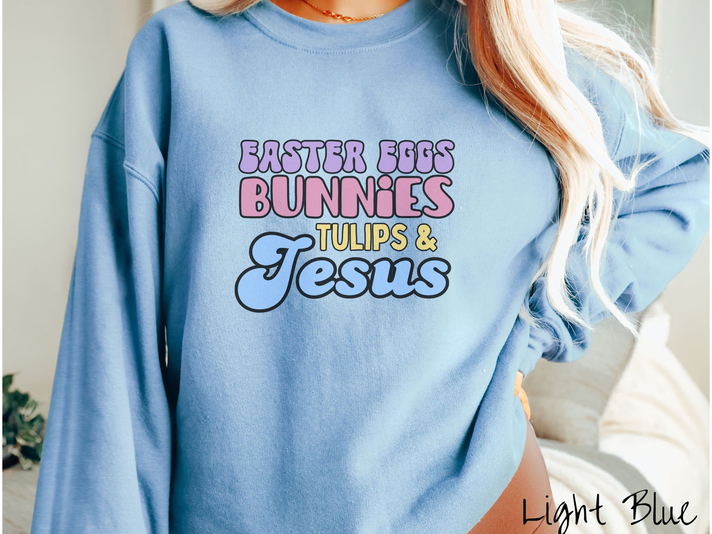 A woman wearing a cute, vintage light blue colored sweatshirt with text Easter Eggs, Bunnies, Tulips, & Jesus in purple, pink, yellow, and blue font.