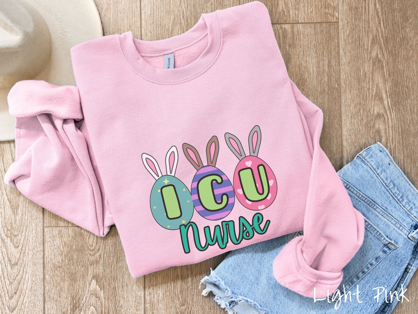 A cute, vintage light pink colored sweatshirt with three colorful easter eggs next to each other with the letters I, C, and U inside. Each egg has a pair of bunny rabbit ears, one is white, the middle brown, and the left gray.