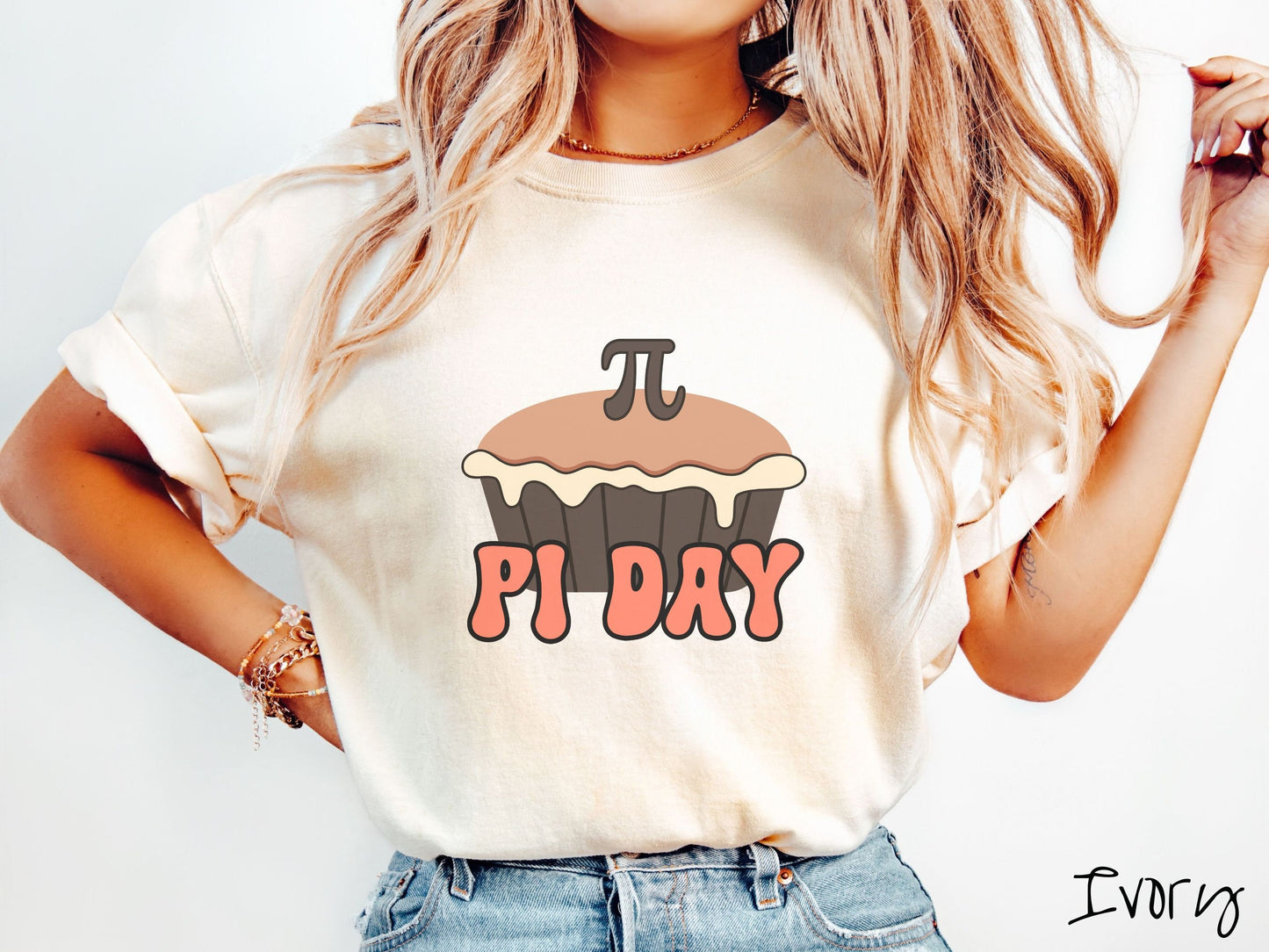 A woman wearing a cute, vintage ivory colored comfort colors shirt with the text Pi Day in orange font, above that is a brown pumpkin pie with a pi symbol on the top of the pie.