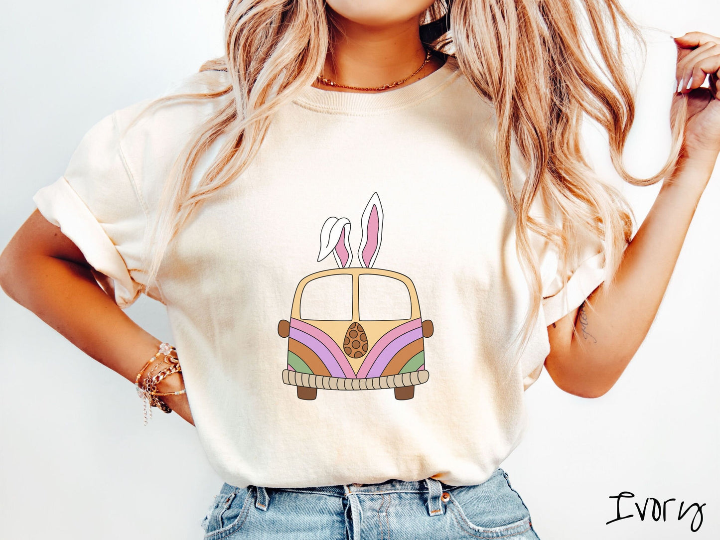 A woman wearing a cute, vintage ivory colored shirt with an old-fashioned, hippie style van with pastel-colored stripes on the front and light orange paint covering the rest. The van has a brown egg on the front and two, floppy bunny ears on top.