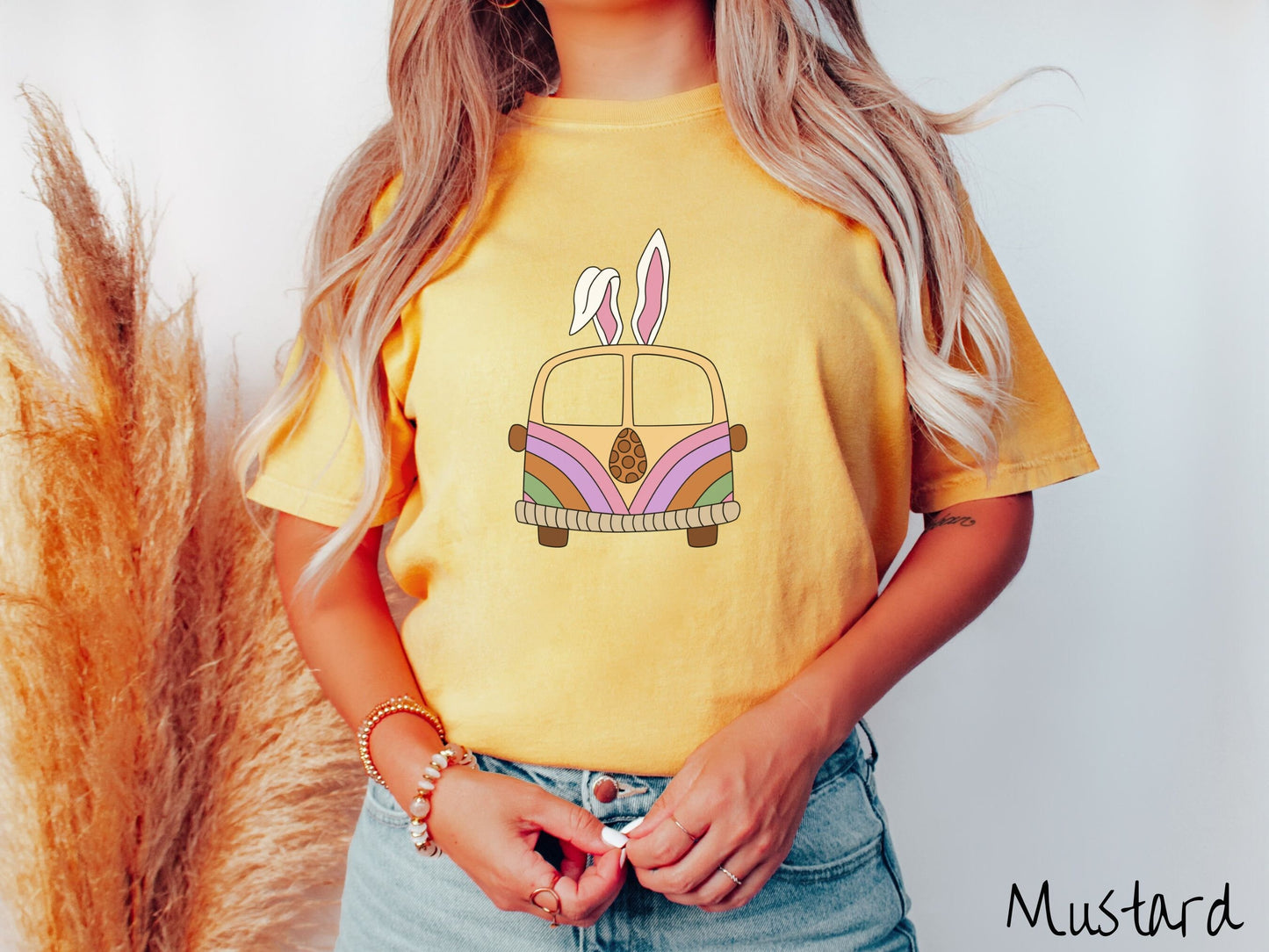 A woman wearing a cute, vintage mustard colored shirt with an old-fashioned, hippie style van with pastel-colored stripes on the front and light orange paint covering the rest. The van has a brown egg on the front and two, floppy bunny ears on top.