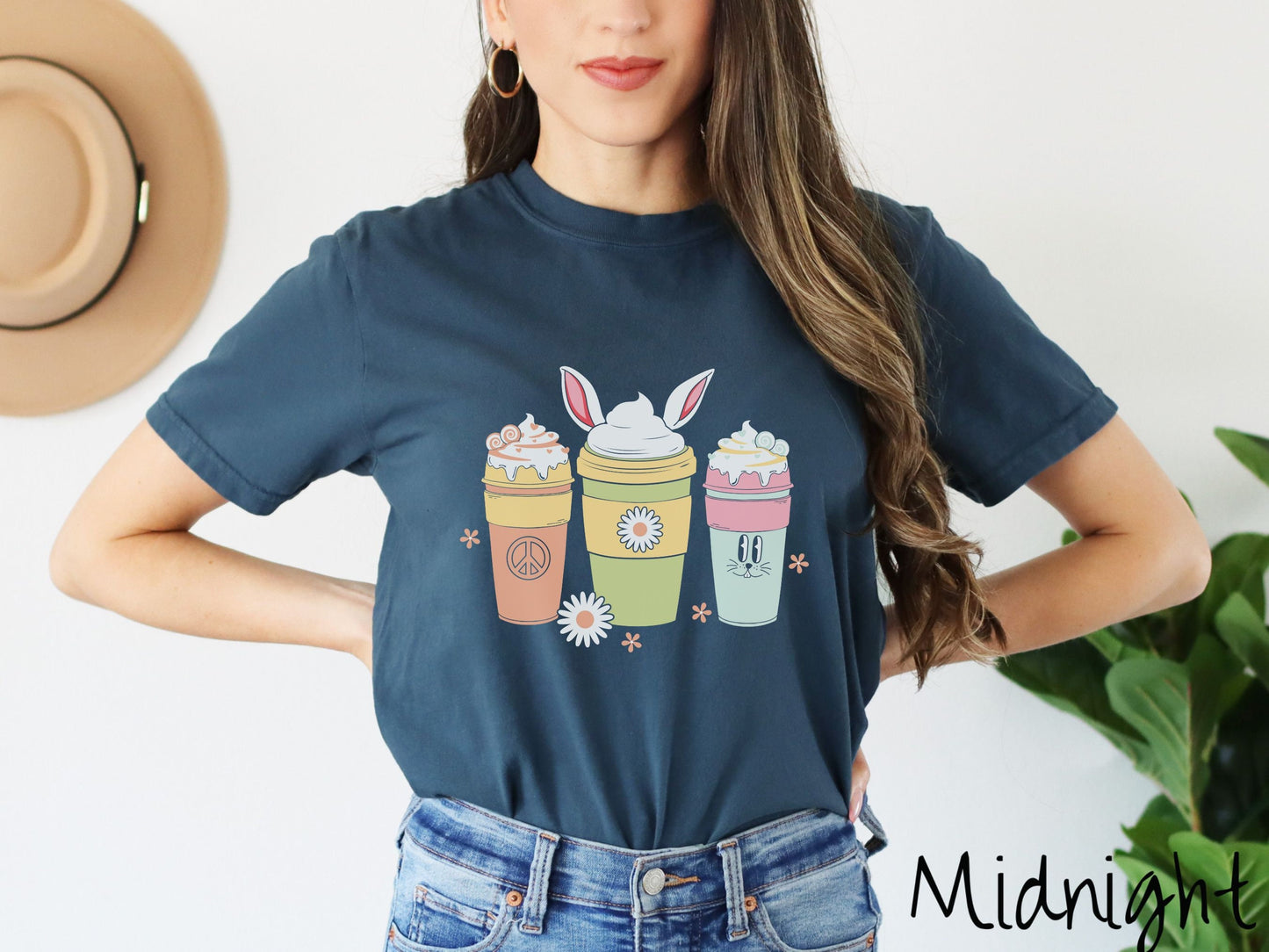 A woman wearing a cute, vintage midnight colored shirt with three coffee cups on the front. One is orange with whipped cream and a peace sign. The middle is green with whipped cream, and bunny ears, and the third is light blue with whipped cream.