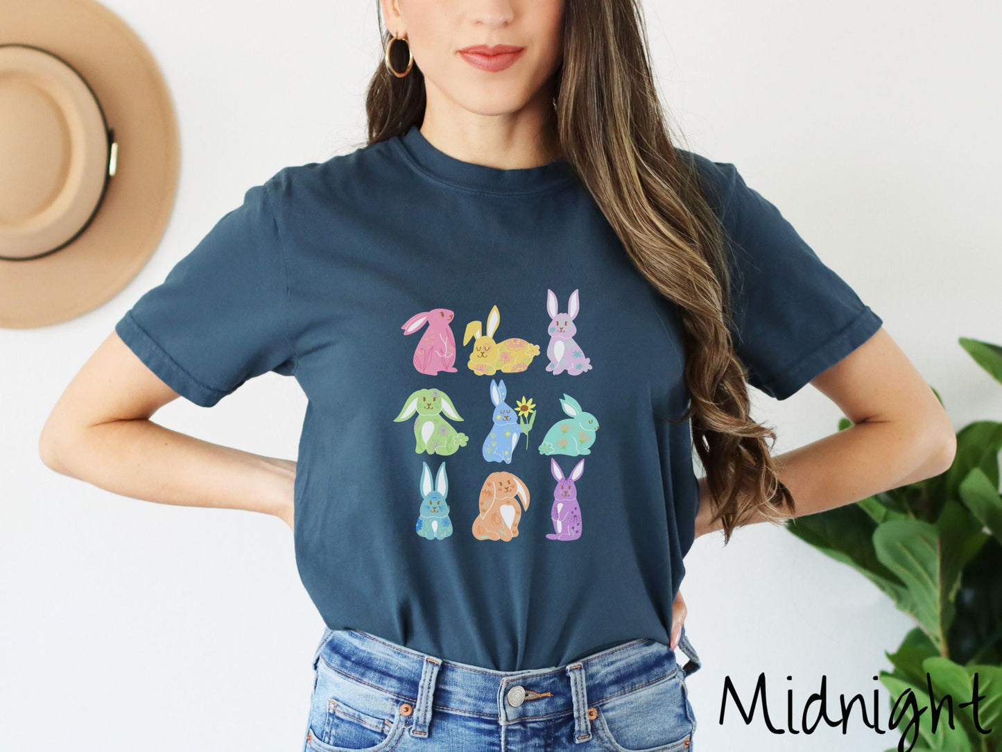 A woman wearing a cute, vintage midnight colored shirt with a three by three grid of colorful bunny rabbits. They are left to right pink, yellow, purple, green, blue, seafoam, light blue, orange, and purple and have flowers and plants drawn on them.