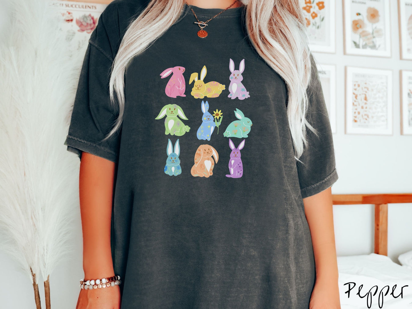 A woman wearing a cute, vintage pepper colored shirt with a three by three grid of colorful bunny rabbits. They are left to right pink, yellow, purple, green, blue, seafoam, light blue, orange, and purple and have flowers and plants drawn on them.