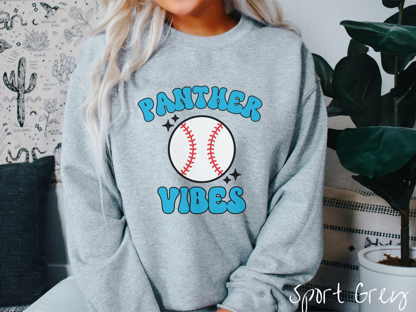 A woman wearing a cute sport grey colored sweatshirt with blue text saying Panther Vibes. There is a white baseball with red stitching between the text.
