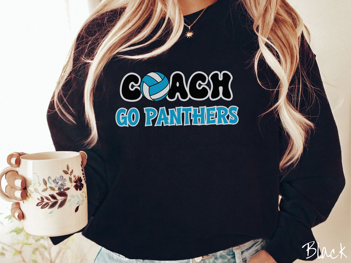 A woman wearing a cute black colored sweatshirt with the word Coach in black and white font, the O in Coach is a blue and white volleyball. Coach Soph are the words in blue and black font Go Panthers.