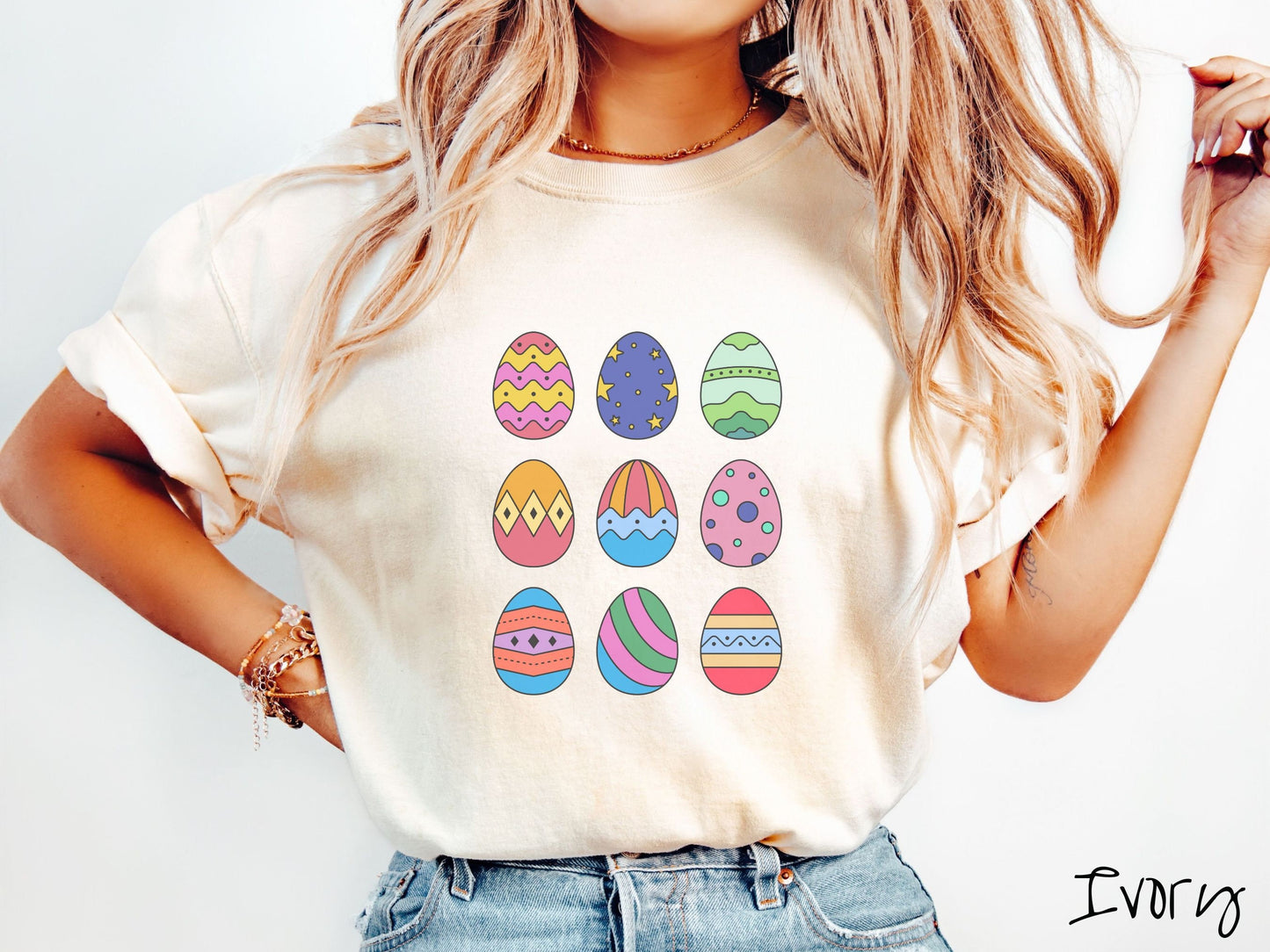 A woman wearing a cute, vintage ivory colored shirt with a three by three grid of colorful Easter eggs. One is pink, red, and yellow, another blue with stars, and another is different shades of green next to five more egg designs.