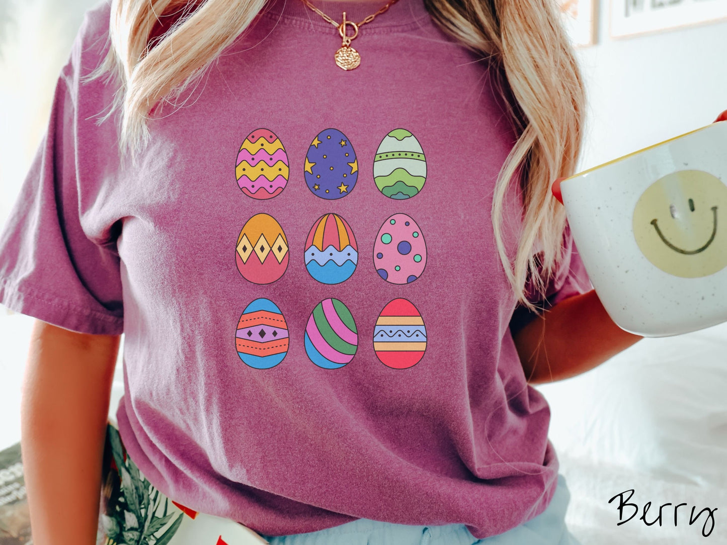 A woman wearing a cute, vintage berry colored shirt with a three by three grid of colorful Easter eggs. One is pink, red, and yellow, another blue with stars, and another is different shades of green next to five more egg designs.